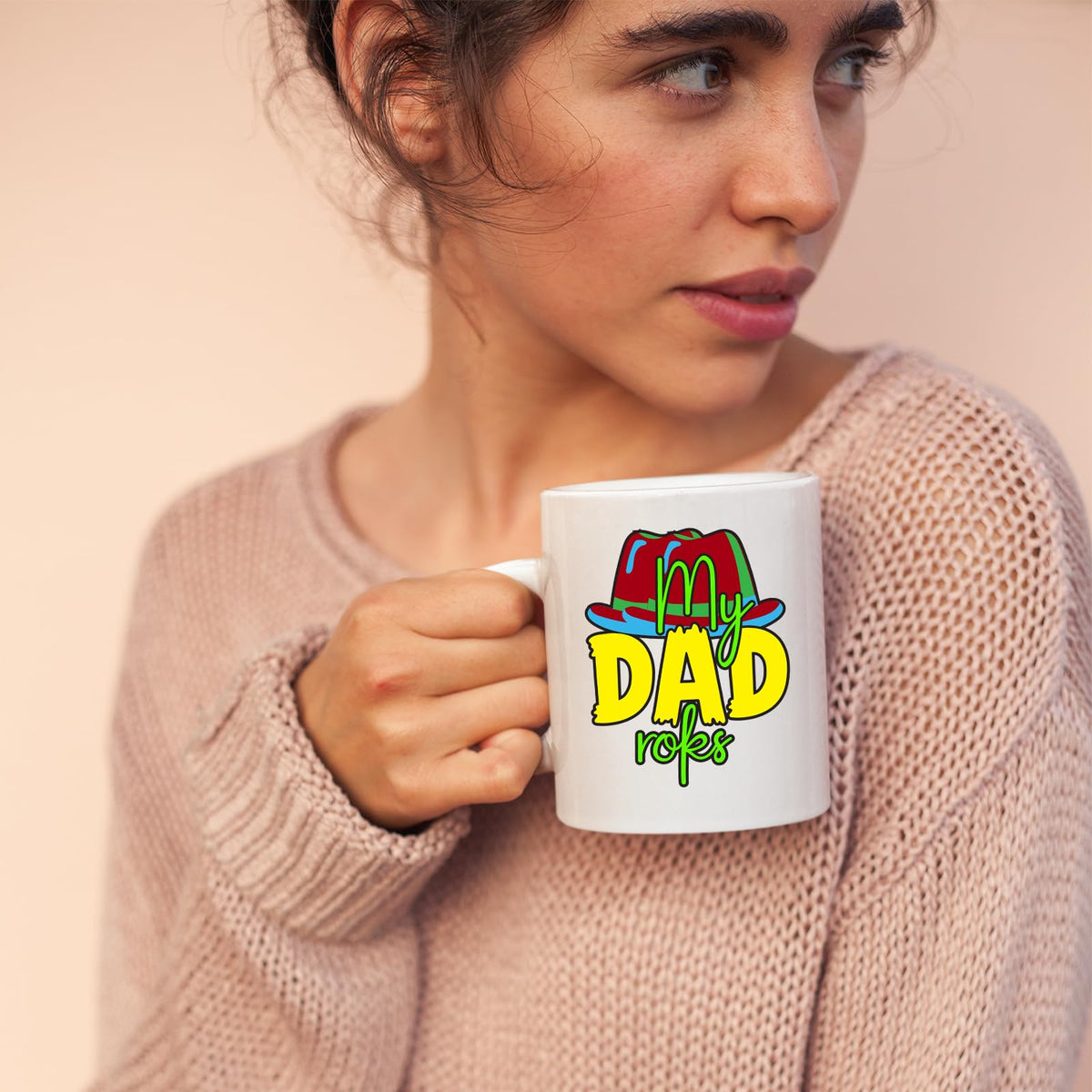 Woman in a pink jumper holding a mug with the colourful My Dad Rocks hat design