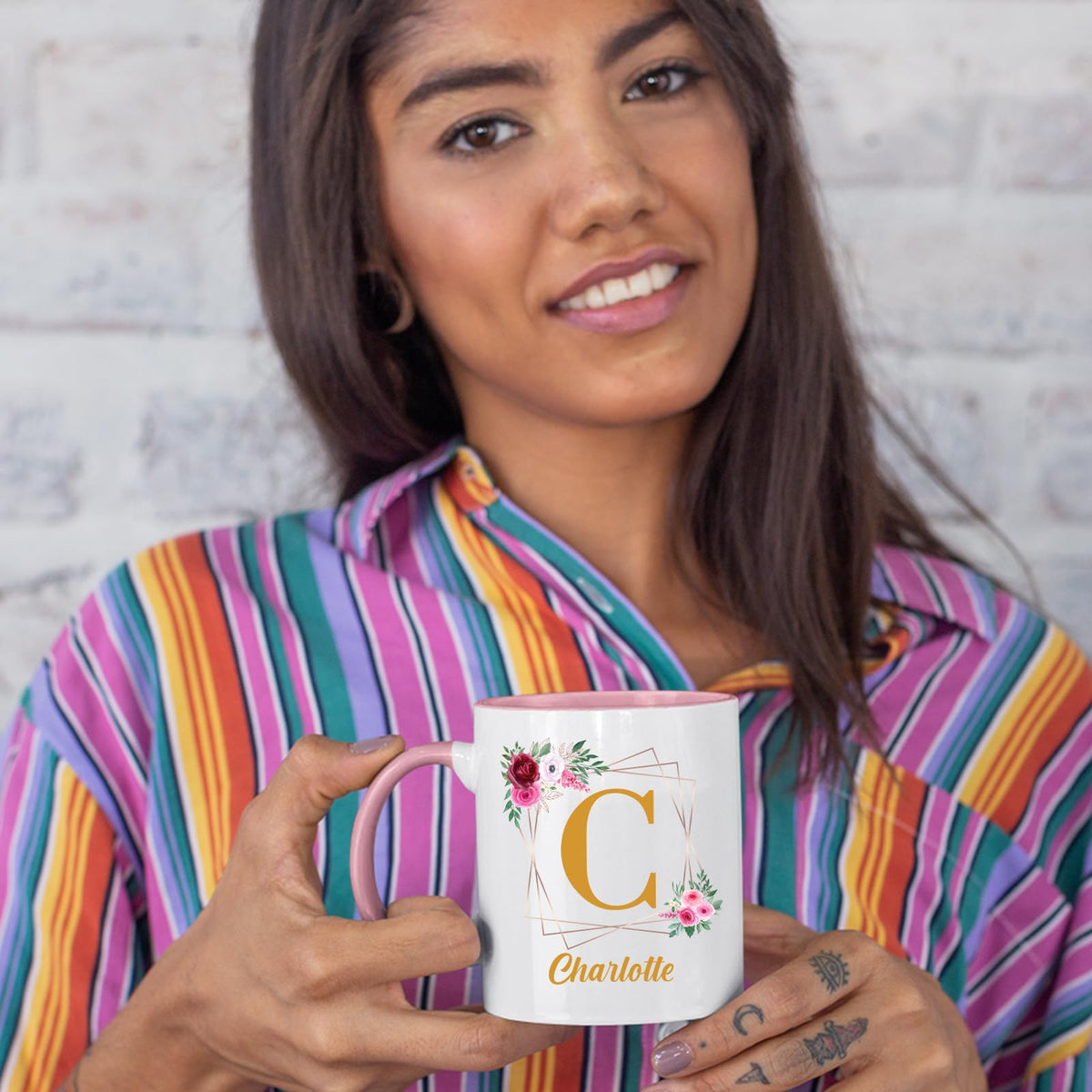 Woman in a striped shirt holding a colour handle mug with a gold initial in a floral frame and an example name