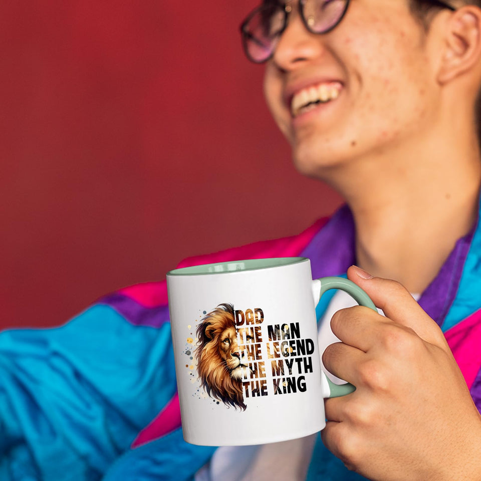 Smiling person in a colourful jacket holding the Dad the King lion mug with a light green handle