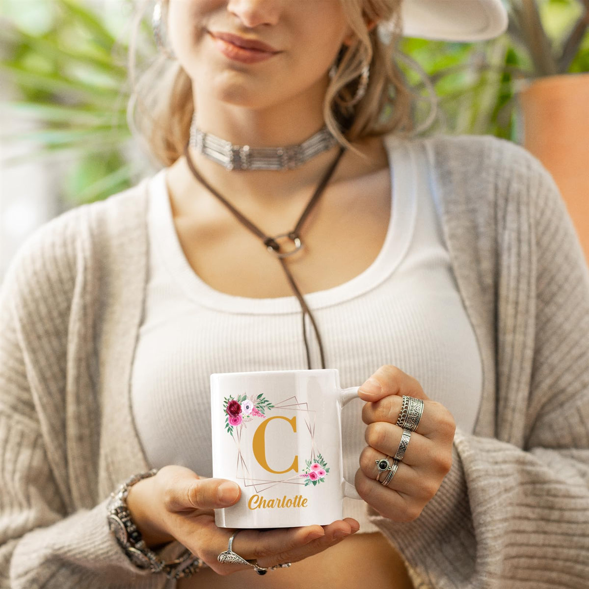 Woman in a cardigan holding a white mug with a gold initial in a floral frame and an example name