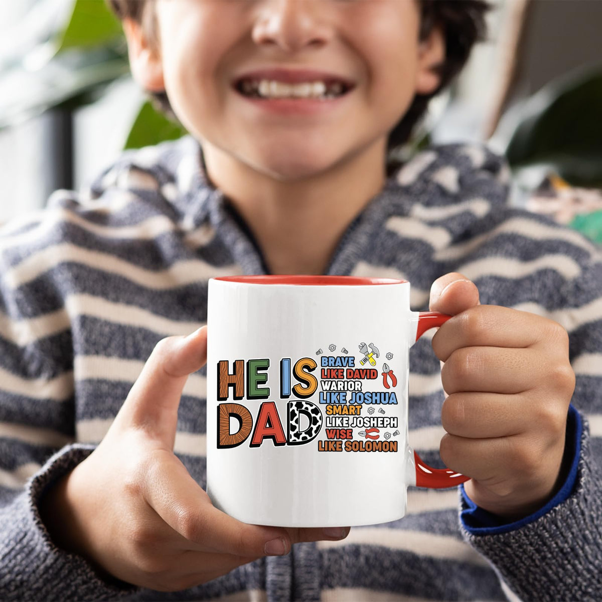 Boy holding a red handle mug with the He Is Dad Bible verse design
