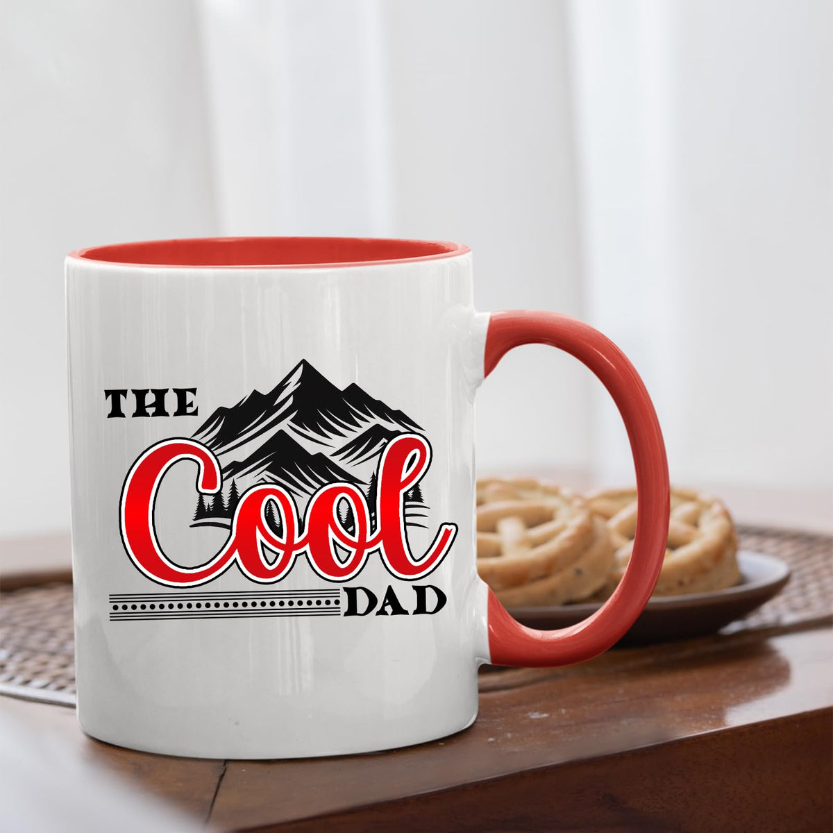 The Cool Dad mountains mug with a red handle beside biscuits