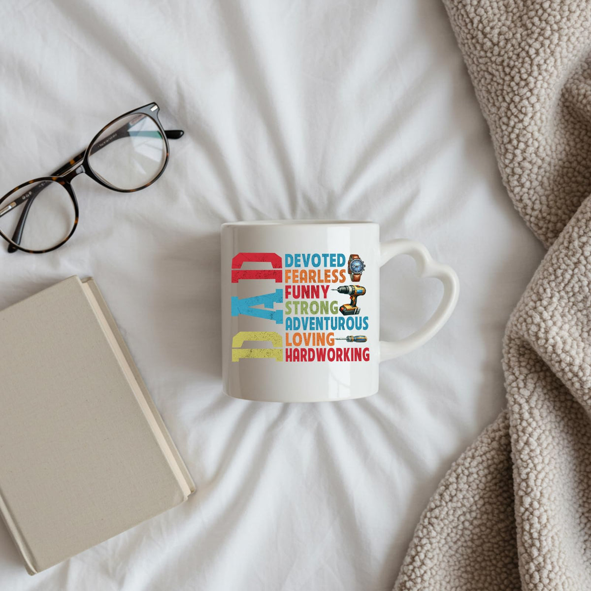 DAD Devoted heart-handle mug on a bed beside glasses and a book