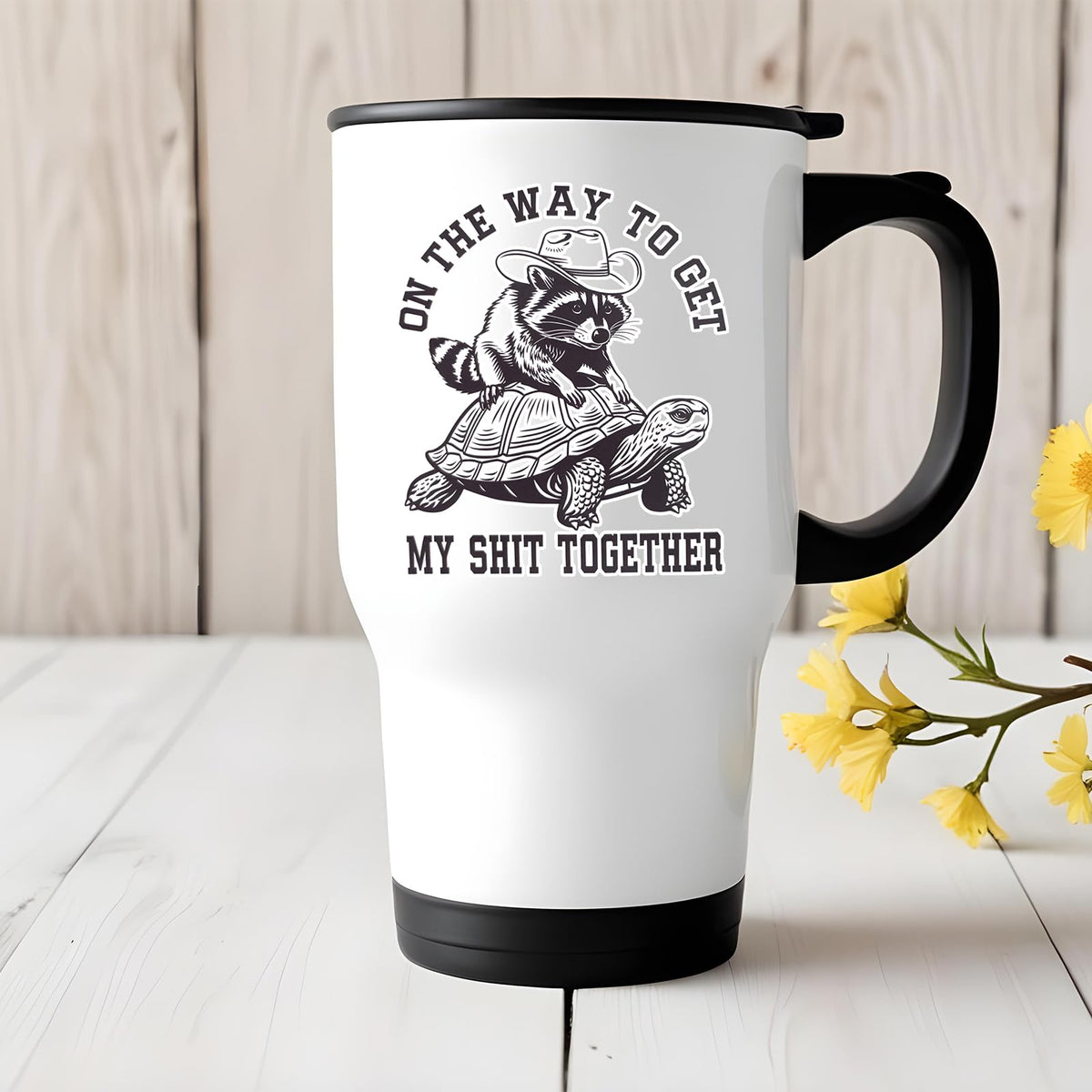 raccoon and tortoise travel mug on a white wooden table with yellow flowers