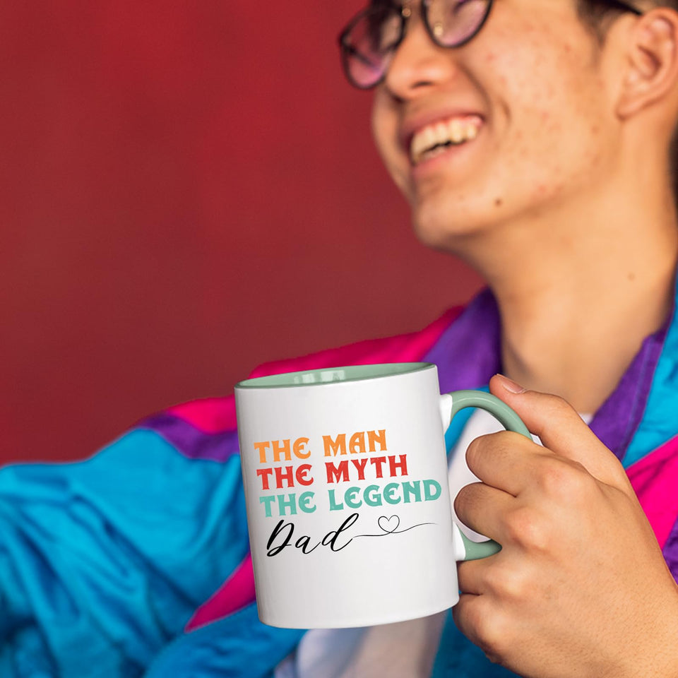 Smiling person in a colourful jacket holding the The Man the Myth Dad mug with a light green handle