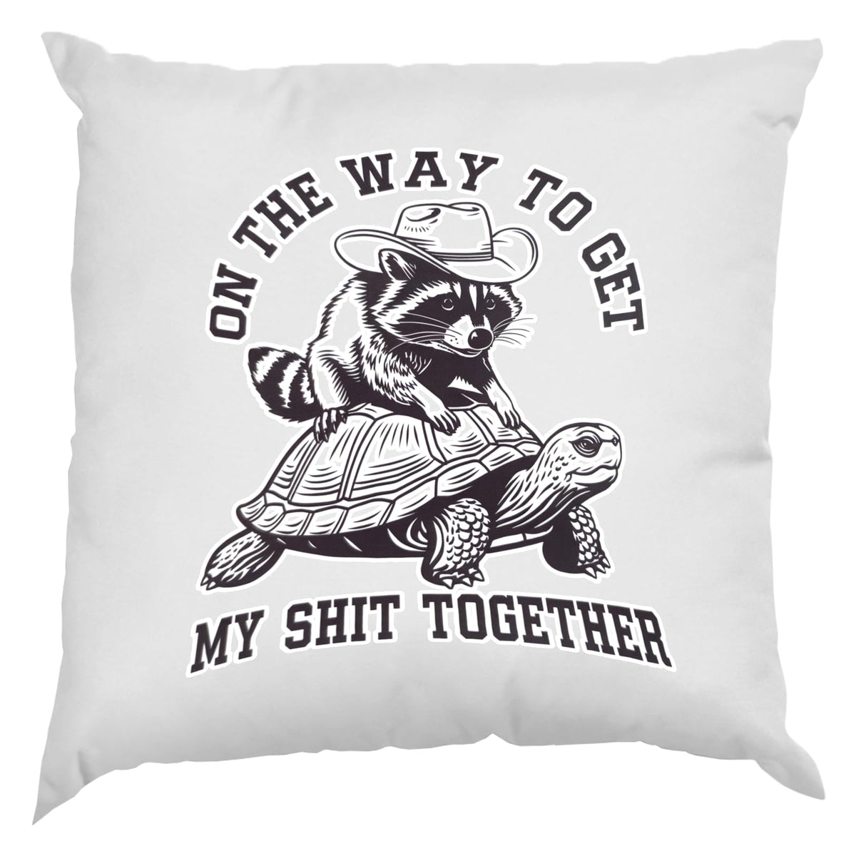 White cushion with a raccoon in a cowboy hat riding a tortoise and “On the way to get my shit together”