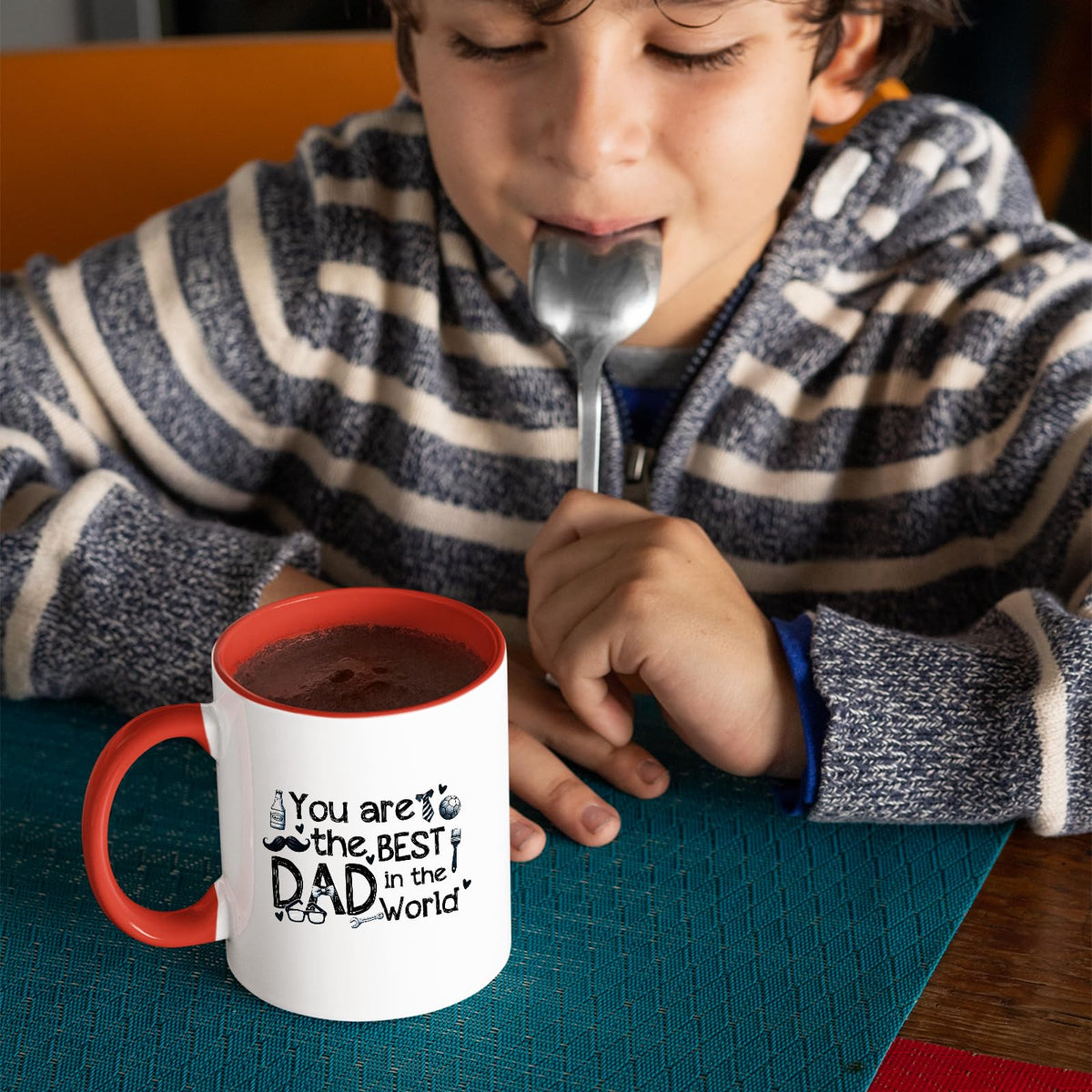 Child with a spoon next to the Best Dad in the World sketch mug with a red handle