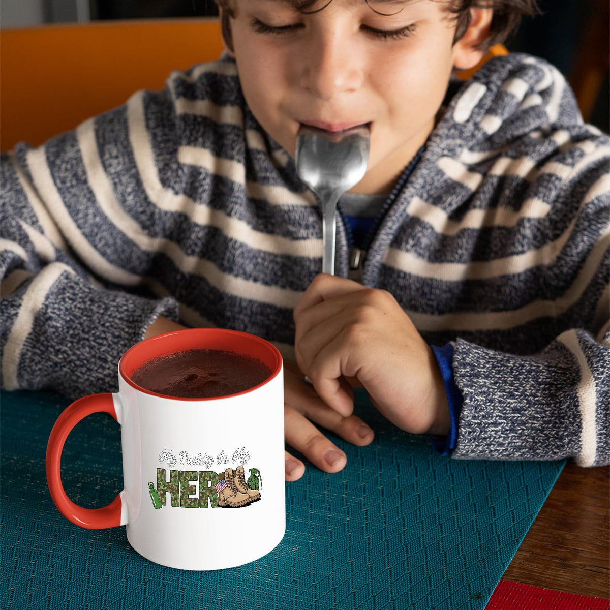Child with a spoon next to the My Daddy Is My Hero military mug with a red handle