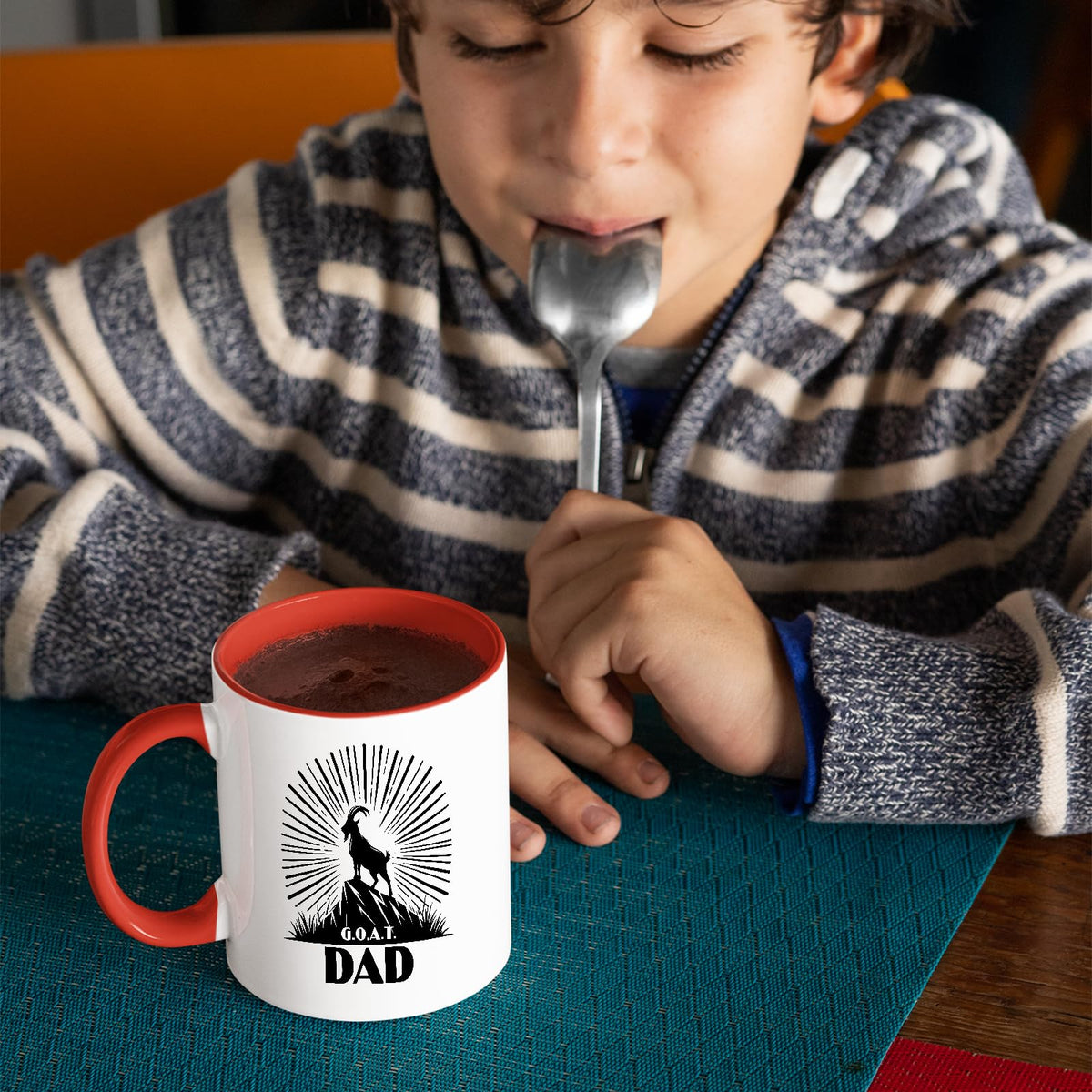 Child with a spoon next to the GOAT Dad mug with a red handle