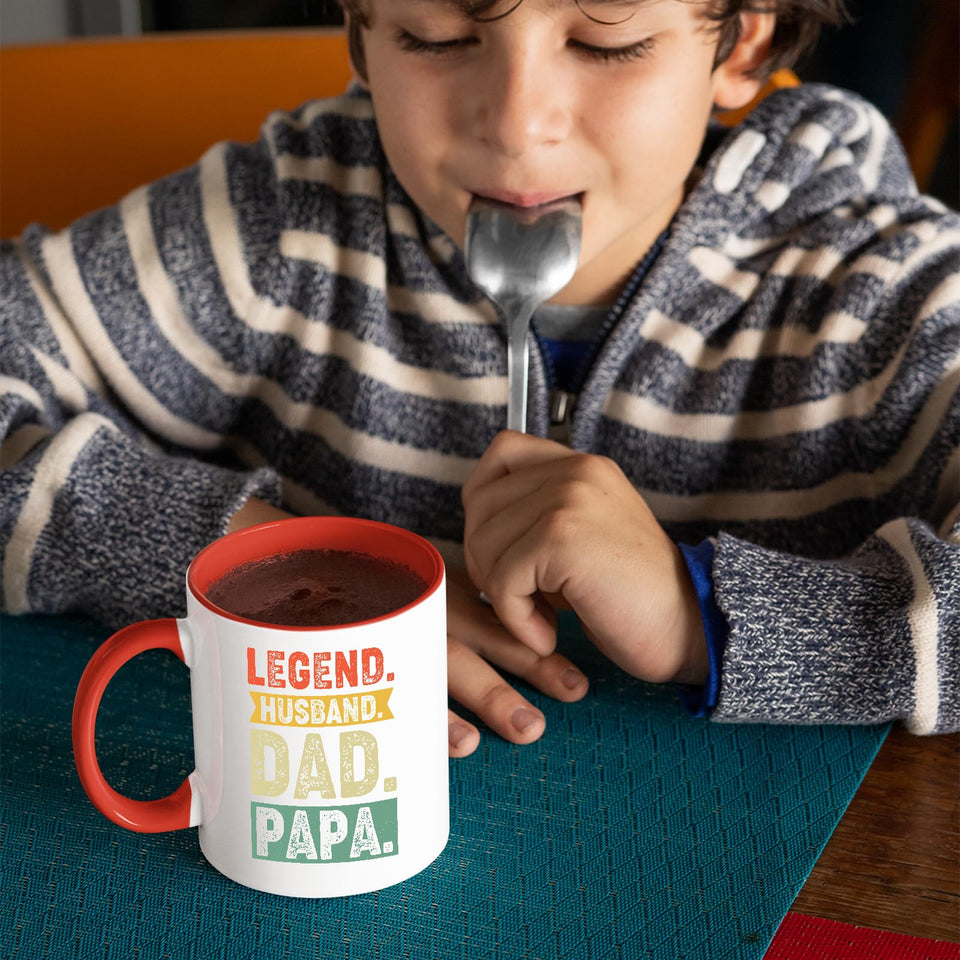 Child with a spoon next to the Legend Husband Dad Papa mug with a red handle