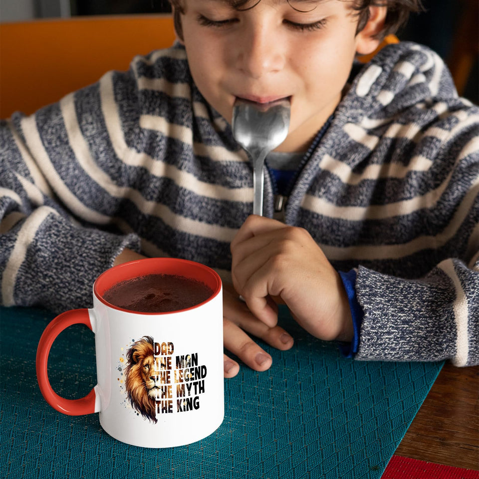 Child with a spoon next to the Dad the King lion mug with a red handle