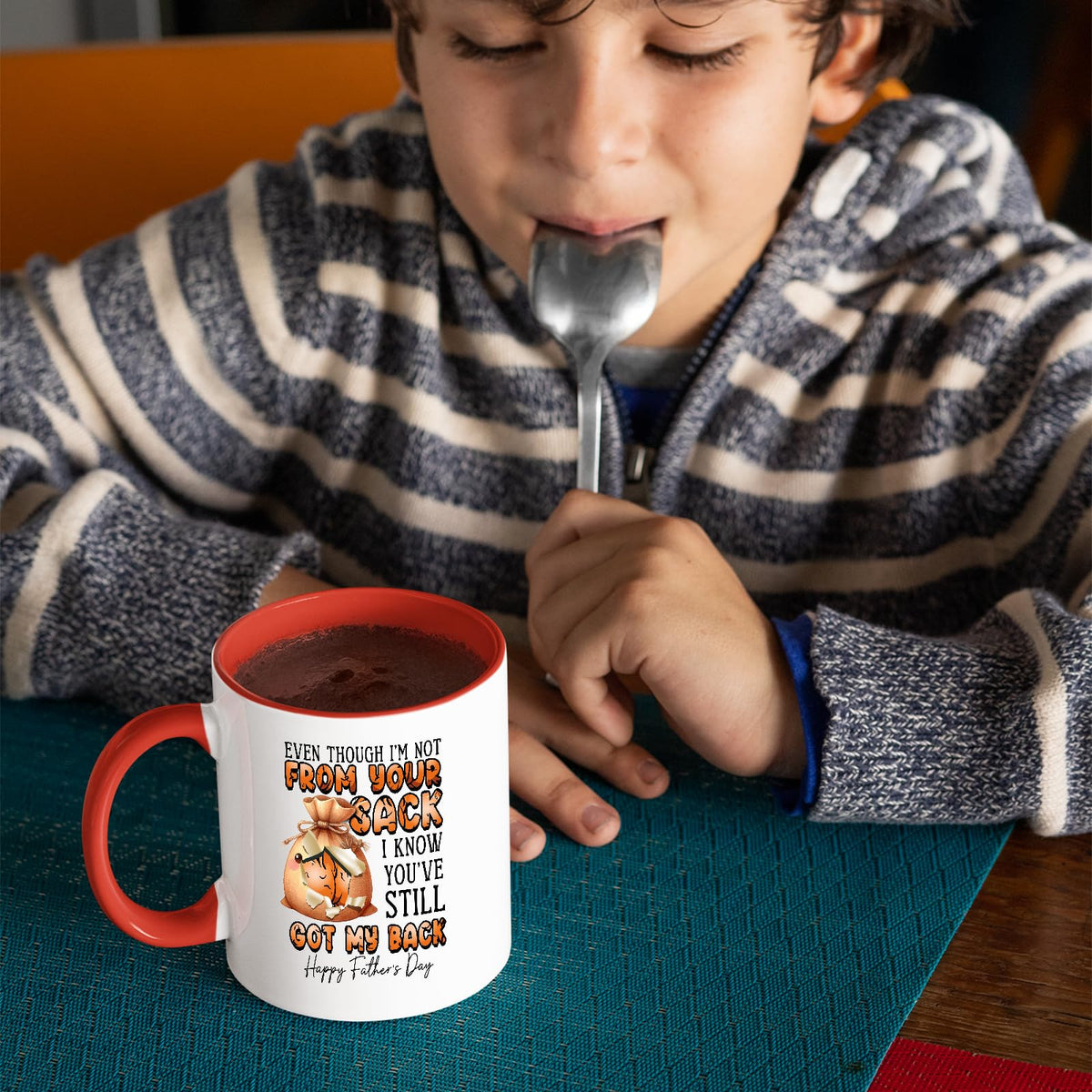 Child with a spoon next to the Not From Your Sack mug with a red handle