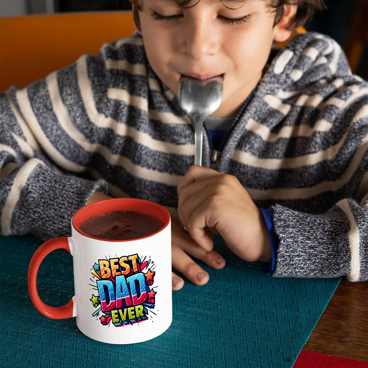 Child with a spoon next to the Best Dad Ever comic mug with a red handle
