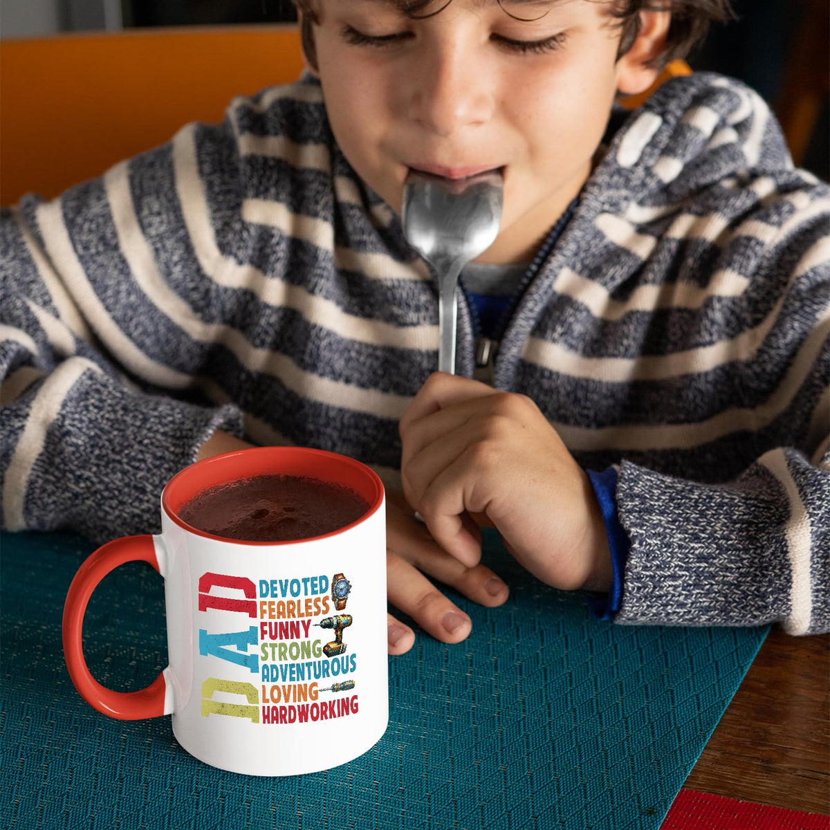 Child with a spoon next to the DAD Devoted mug with a red handle
