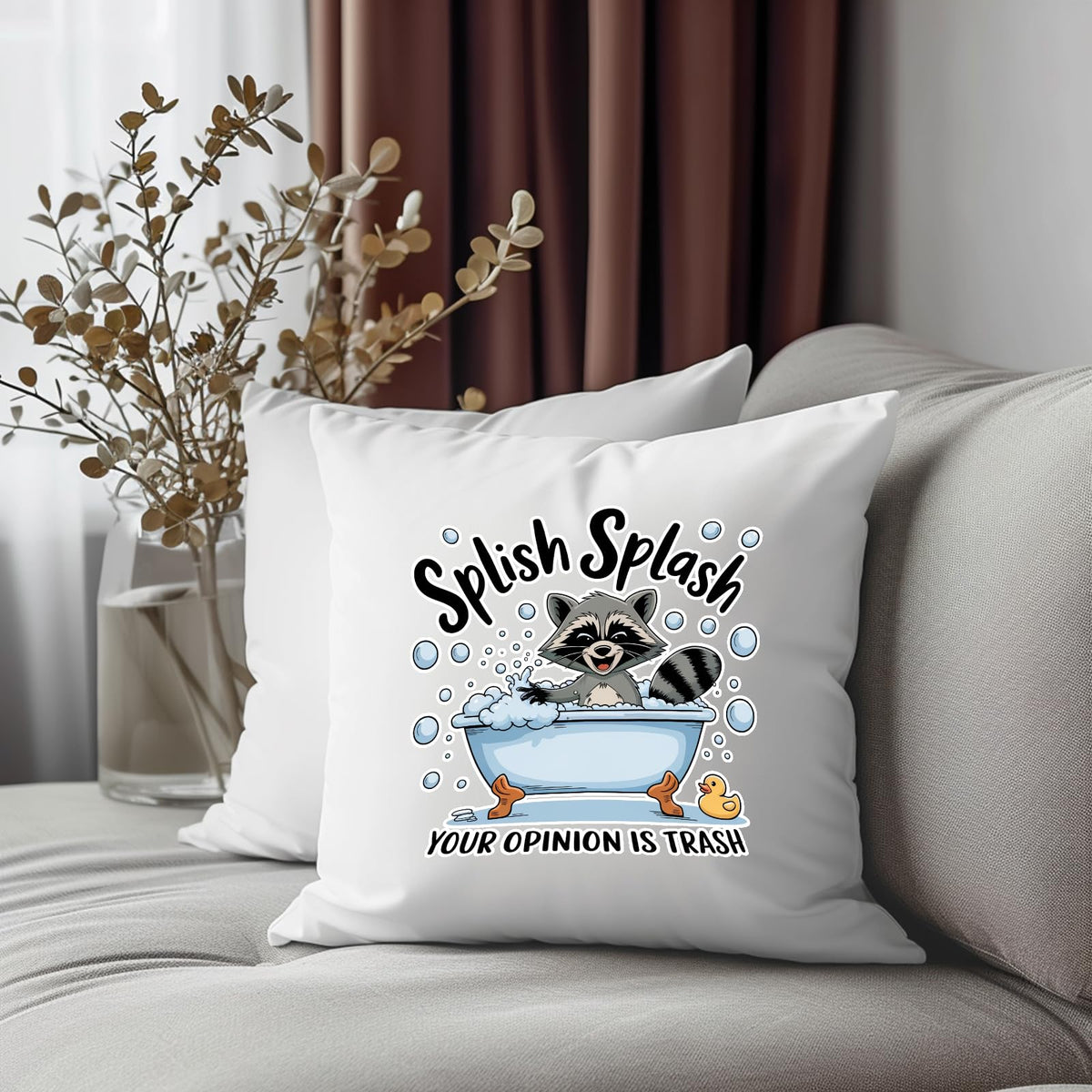 Splish Splash raccoon cushion on a grey sofa beside dried flowers