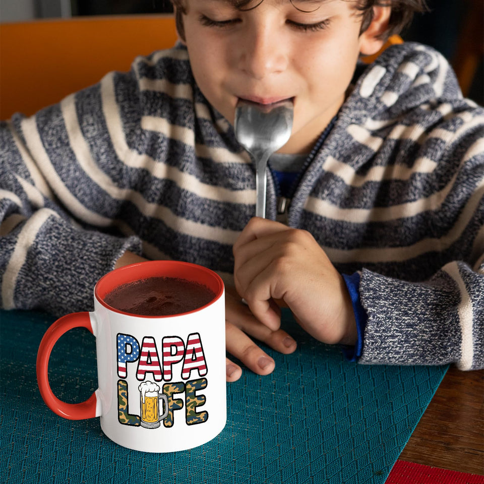 Child with a spoon next to the Papa Life mug with a red handle