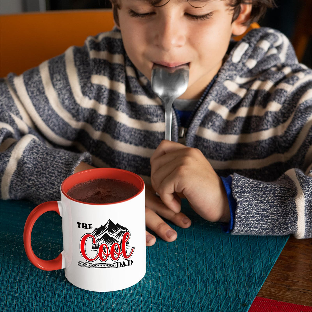 Child with a spoon next to the The Cool Dad mountains mug with a red handle