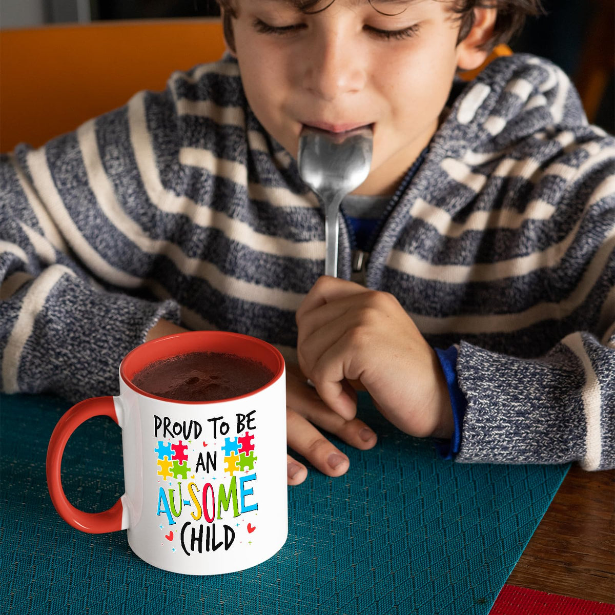 Child with a spoon next to the Proud to Be an Au-Some Child mug with a red handle