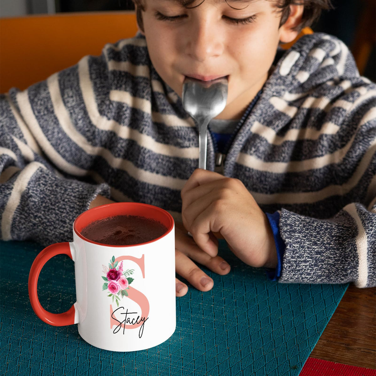 Boy with a spoon next to a red handle mug with a blush pink initial with roses and an example name