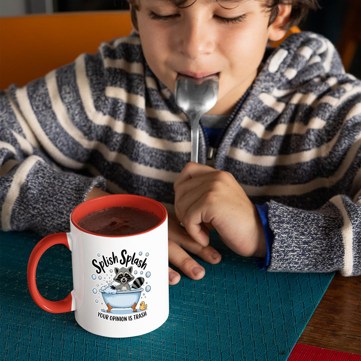 Child with a spoon next to the Splish Splash raccoon mug with a red handle