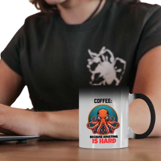 Person holding the colour changing mug with a grumpy octopus and “Coffee: Because Adulting Is Hard”