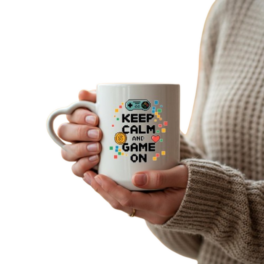 Hands holding the heart-handle mug with “Keep Calm and Game On” with a game controller
