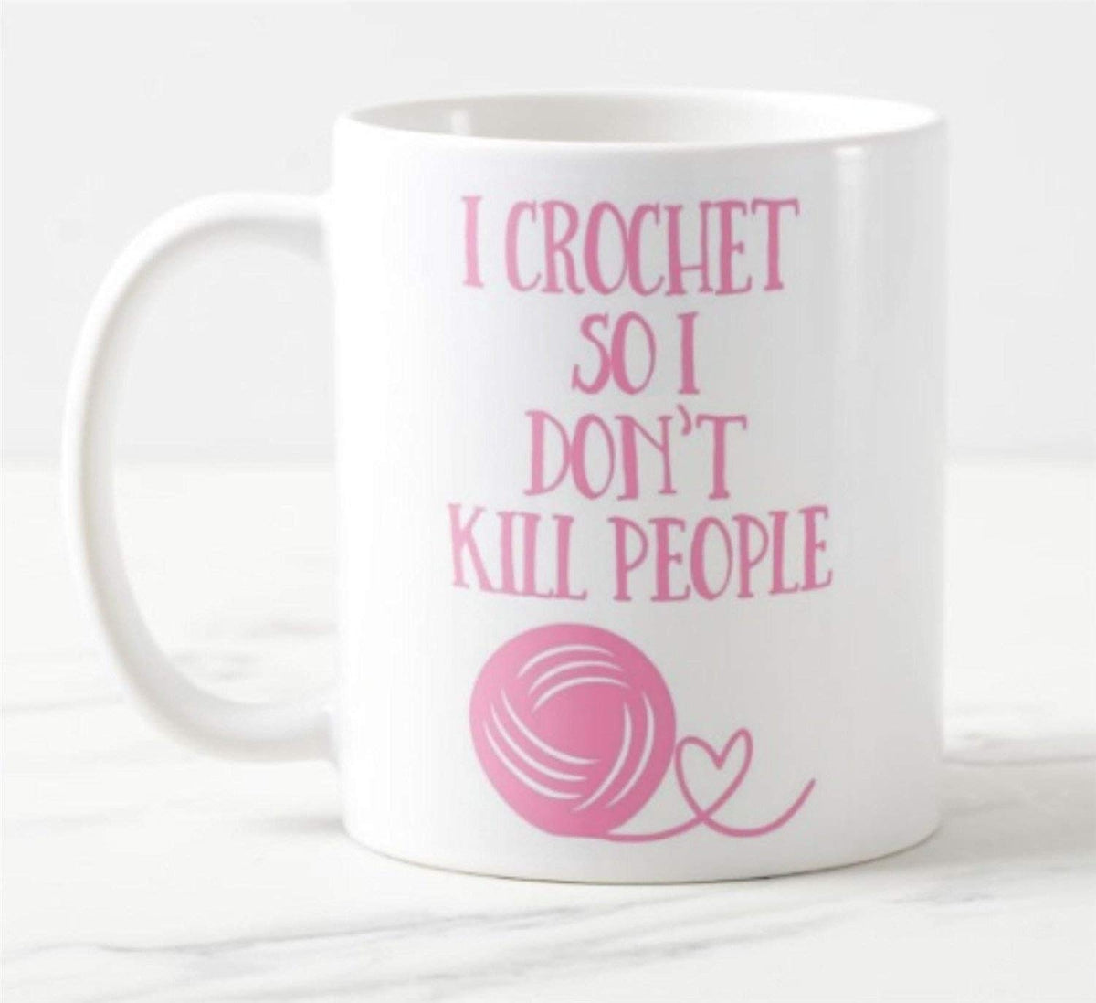 White mug printed with “I Crochet So I Don't Kill People” in pink with a ball of yarn