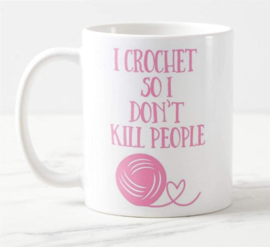 White mug printed with “I Crochet So I Don't Kill People” in pink with a ball of yarn
