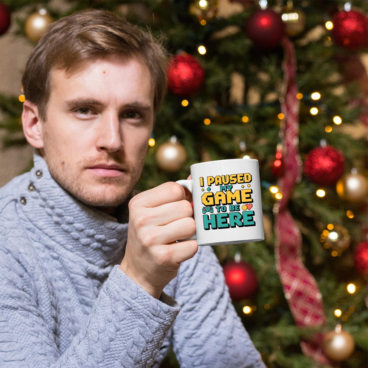 Man holding the I Paused My Game mug by a Christmas tree